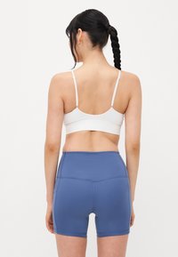 Bralette blanc à côtes avec bretelles réglables, associé à un short en jean ajusté et taille haute de couleur bleu clair avec des coutures décoratives.