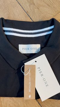 Črna polo majica iz recikliranega bombaža, z belim ovratnikom z nasprotno črto. Na etiketah piše "PIER·ONE." Priložene oznake.
