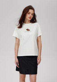 White cotton t-shirt with short sleeves, featuring an orange and black butterfly graphic and text "GOOD THINGS ARE COMING" below it.