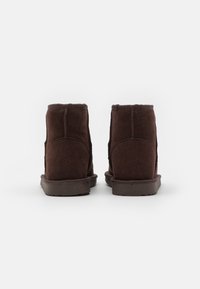 Brown suede ankle boots with a soft texture, round toe, flat rubber sole, and stitched detailing on the back and sides.