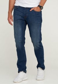 Mörkblå denimjeans med smal passform, femficksdesign och subtila blekningsdetaljer. Bärs med vita sportskor och en vit t-shirt.