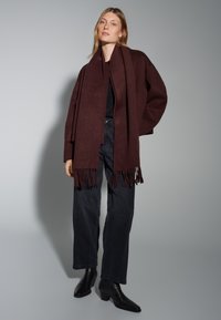 Burgundy wool scarf with fringe edges, draped over a black fitted top, paired with black wide-leg jeans and ankle boots.