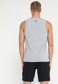 Top sin mangas de algodón gris con cuello redondo, tirantes, y un logo negro en la parte posterior, combinado con pantalones cortos negros.