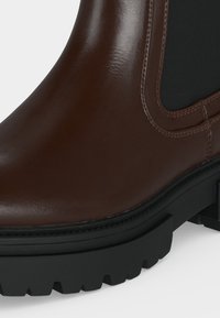 Gros plan d'une botte en cuir marron avec un panneau latéral élastique noir et une semelle épaisse, noire et robuste.