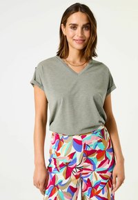 Camiseta gris de cuello en V con mangas enrolladas, combinada con pantalones de floral colorido con acentos en rojo, azul y beige. Textura suave.