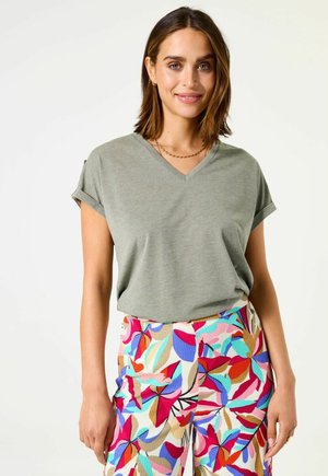 Grijze v-hals t-shirt met opgerolde mouwen, gecombineerd met kleurrijke bloemenpatroonbroeken met rode, blauwe en beige accenten. Soepele textuur.