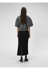 Graues Oberteil mit Puffärmeln und rundem Halsausschnitt, kombiniert mit einem schwarzen Midirock mit einem Schlitz hinten und schwarzen High-Heels.