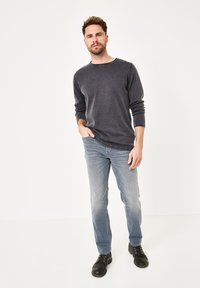 Dunkelgraues Langarmshirt mit Rundhalsausschnitt, kombiniert mit hellblauen Slim-Fit-Jeans und schwarzen Schnürstiefeln vor einem weißen Hintergrund.