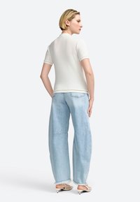 Leichte, cremefarbene Poloshirt mit kurzen Ärmeln, kombiniert mit übergroßen hellblauen Jeans, die fransige Säume und dezente Abnutzung aufweisen.