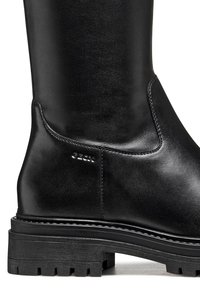 Bota negra de cuero hasta la rodilla con suela de goma gruesa y diseño minimalista, con costuras sutiles y detalle del logo en el lateral.