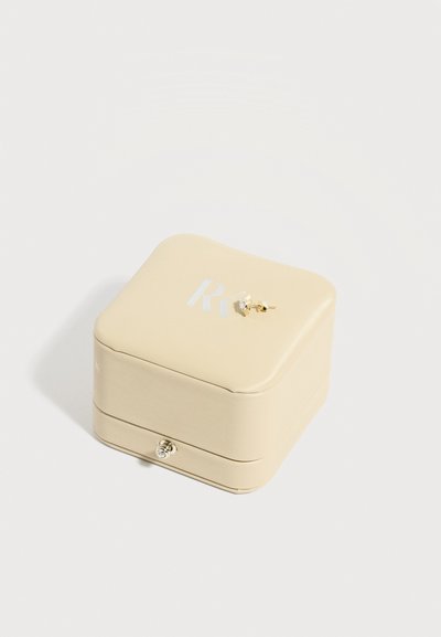 Μικρό μπεζ δερμάτινο κουτί κοσμημάτων με ασημένιο κούμπωμα, στολισμένο με ένα μόνο χρυσό σκουλαρίκι με διαμάντι.