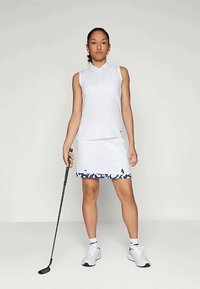 Balta bezpiedurkņu polo krekls, kas apvienots ar baltu svārku ar zilu ziedu rakstu apakšmalā. Figūra tur golfa nūju, zīmējot baltas sporta kurpes.