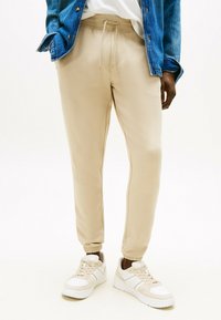 Beige sweatpants met een tapered fit, elastische tailleband en boorden, gecombineerd met witte sneakers met beige accenten en een gestructureerd oppervlak.