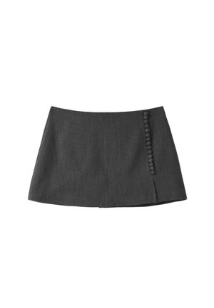 Femme portant un haut noir sans manches, une mini-jupe gris foncé, des chaussettes blanches, des chaussures noires et un pull gris posé sur ses épaules.