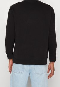 Felpa nera con maniche lunghe, polsini e orlo a costine. Tessuto in misto cotone con una texture liscia, indossata con jeans azzurri chiari.