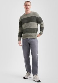 Grijze en groene gestreepte gebreide trui met een geribbelde textuur, gecombineerd met lichtgrijze jeans en neutrale sportschoenen. Minimalistische outfitstijl.