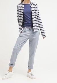 Pasiasty granatowo-biały kardigan na gładkiej granatowej bluzce, w połączeniu z jasnoniebieskimi spodami z podwiniętymi nogawkami i białymi trampkami. Gładkie tekstury.