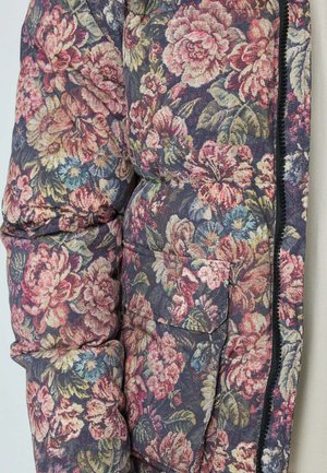 Doudoune florale avec des fleurs violettes, roses et vertes. Design matelassé, poche avant et détails de fermeture éclair noire. Tissu texturé.