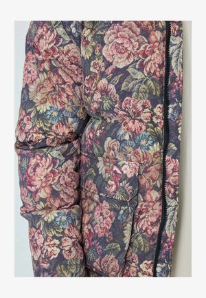 Doudoune florale avec des fleurs violettes, roses et vertes. Design matelassé, poche avant et détails de fermeture éclair noire. Tissu texturé.