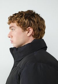 Czarna kurtka puchowa z wysokim kołnierzem i zapięciem na zamek. Gładka, matowa tekstura z pikowanym przeszyciem na ramionach.