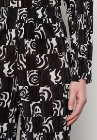 Tecido com padrão em preto e branco, com textura ribada, apresentando designs abstratos em quadrados contrastantes, usado em uma peça de vestuário ajustada.