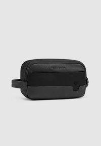 Zwarte toilettas met een gestroomlijnde rechthoekige vorm, voorzien van een mix van getextureerd leer en glad synthetisch materiaal. Ritssluiting en zijhandvat.