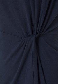 Mörkblå klänning i mjukt jersey-material med rynkade detaljer vid midjan som skapar en vriden knoteffekt. Slät yta och figurnära passform.