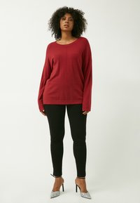 Maglione rosso a maniche lunghe con vestibilità comoda, caratterizzato da un collo arrotondato e cuciture lavorate, abbinato a pantaloni neri aderenti e tacchi argentati.