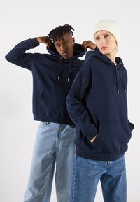 Mørkeblå hettegensere med snor og frontlommer, laget av myk stoff. Kombinert med lyseblå denimbukser.