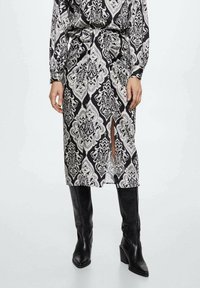 Robe à motifs noir et blanc avec une fente, fabriquée en tissu doux. Caractéristiques : manches longues et taille ceinturée, associée à des bottes noires montantes.