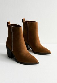 Brązowe zamszowe botki za kostkę z szpiczastymi noskami i zamkami błyskawicznymi po bokach, z czarnym słupkiem i pętelką z tyłu dla łatwego zakładania.