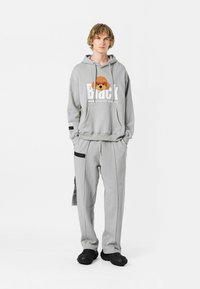 Sudadera gris con un gráfico de un oso y texto blanco, combinada con pantalones joggers grises a juego con acentos negros y bolsillos. Calzado negro.