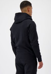 Zwarte hooded sweatshirt met een zachte textuur, met een aansluitend ontwerp en geribbelde manchetten. De achterkant heeft een schone naad en een minimalistische stijl.