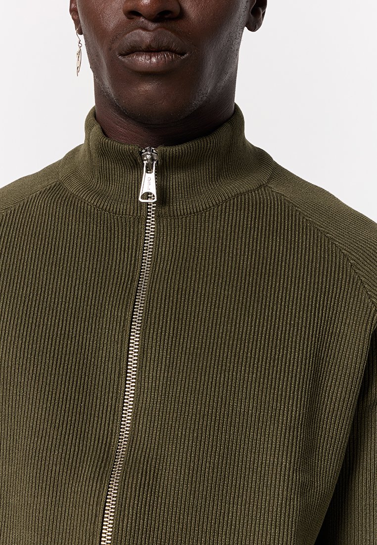 Giacca zip-up verde oliva con colletto alto, texture a coste e dettagli in zip argentata nella parte anteriore. Design aderente.
