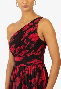 Robe asymétrique noire avec des motifs floraux rouges ; corsage plissé et jupe fluide. Tissu texturé avec taille cintrée et silhouette décontractée.