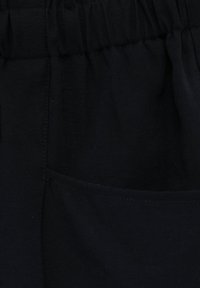 Tessuto nero con una texture liscia, caratterizzato da una vita arricciata e una tasca laterale funzionale. Le cuciture sono visibili lungo le giunture.