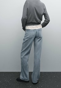 Vaaleansiniset farkut, joissa on suora lahje, viisi taskua ja hieman kulunut pinta. Yllä harmaa neule, joka on kerrottu valkoisen paidan päälle.