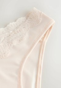 Sous-vêtements rose clair avec une délicate bordure en dentelle florale le long de la ceinture sur un fond uni clair.