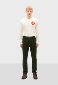 Weißes Langarmhemd mit einem roten Muschel-Graphic, kombiniert mit dunkelgrünen Cordhosen und braunen Schnürschuhen. Einfaches Design, strukturierter Stoff.