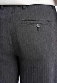 Pantaloni grigi con motivo pied-de-poule, dotati di tasca posteriore e chiusura a bottone. Il tessuto presenta una finitura texturizzata e la vita sembra ben rifinita.