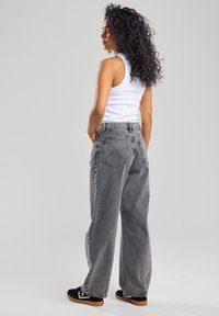 Gray wide-leg jeans feature a high waist, classic five-pocket design, and a faded wash, paired with a white tank top and black sneakers.