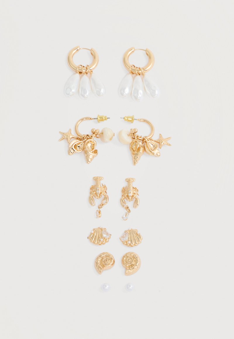 Six paires de boucles d'oreilles en ton or avec des charms sur le thème de la mer, comprenant des perles, des coquillages, des étoiles de mer et des homards, disposées sur un fond blanc.