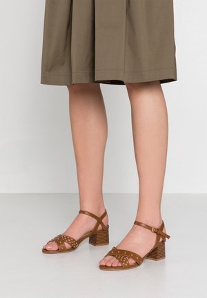 Czarne skórzane sandały na obcasie z ćwiekowanymi akcentami, z otwartym przodem, regulowanymi paskami w kostce i blokowym obcasem o teksturowanej powierzchni.