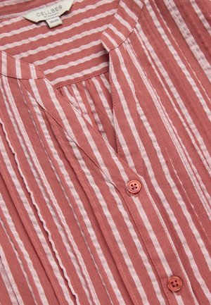 Rustfarvet lyserød bluse med vertikale hvide striber, rund krave, to synlige knapper og en plisseret detalje under halsudskæringen.