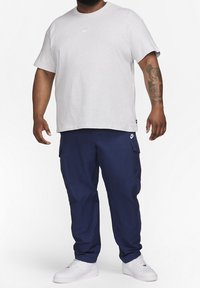 Ljusgrå bomullströja med korta ärmar och en liten logotyp på bröstet, kombinerad med marinblå cargobyxor med sidofickor. Vita sneakers.