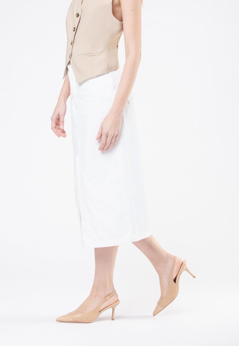 Gilet sans manches beige avec des boutons, associé à une jupe midi blanche et des escarpins à bride arrière en vernis nude avec un bout pointu et un talon fin.