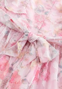 Floral Kleid aus transparentem pinkem Stoff, mit einer Schleife in der Taille, rüschigem Muster und einem bunten Blumenmuster. 