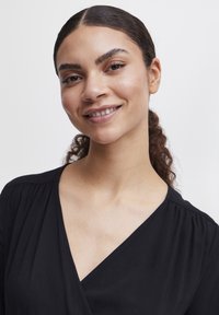 Top noir enroulé avec un décolleté en V et des manches courtes. Tissu doux avec une texture subtile, offrant une coupe décontractée au niveau des épaules.