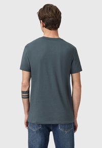 Camiseta de algodón gris con mangas cortas, cuello redondo y una textura suave. Mostrada por la parte de atrás, llevada con jeans de denim azules.