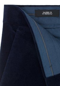 Granatowe spodnie kordowe z gładką niebieską podszewką. Posiadają metkę z napisem "DOPASOWANE IDEALNIE." Widoczna szczegółowa przeszycia.